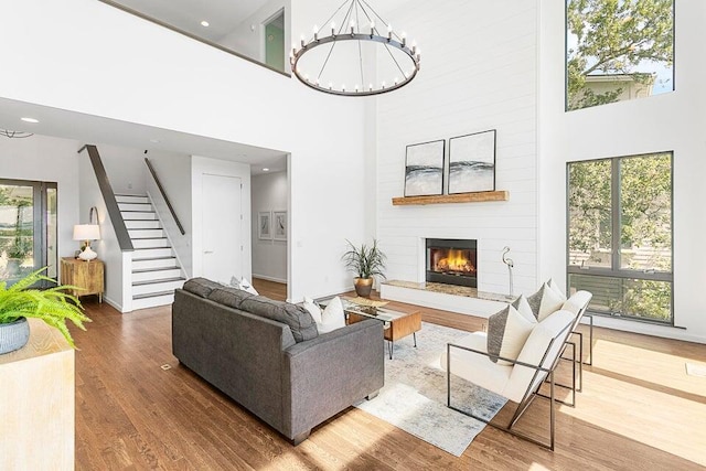 living room featuring hardwood / wood-style floors, a notable chandelier, a large fireplace, and a high ceiling