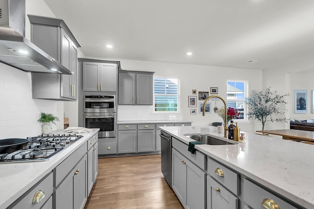 kitchen featuring gray cabinets, sink, stainless steel appliances, and wall chimney range hood