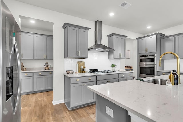 kitchen featuring light stone countertops, appliances with stainless steel finishes, wall chimney exhaust hood, sink, and gray cabinets