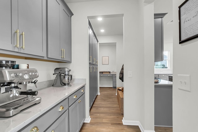 bar featuring gray cabinets, light stone counters, and light hardwood / wood-style floors