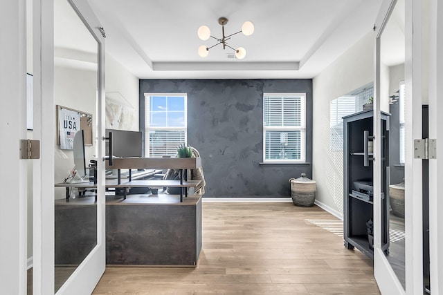 office area with light wood-type flooring, an inviting chandelier, and a raised ceiling