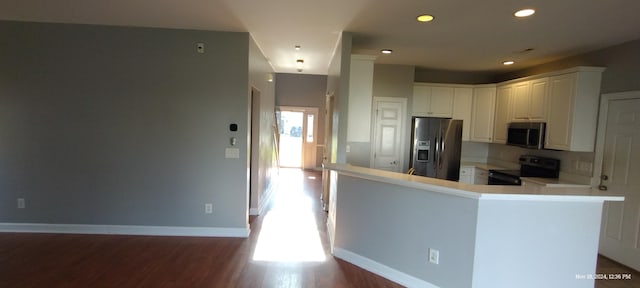 kitchen with kitchen peninsula, backsplash, stainless steel appliances, wood-type flooring, and white cabinets