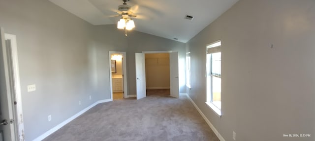 unfurnished bedroom featuring lofted ceiling, light carpet, a walk in closet, connected bathroom, and a closet