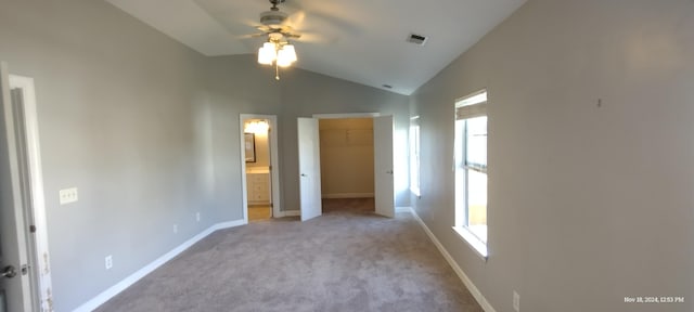 unfurnished bedroom featuring lofted ceiling, a walk in closet, ensuite bath, light colored carpet, and a closet