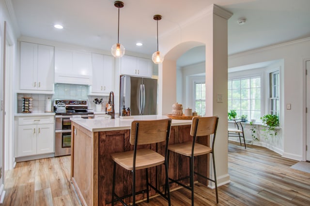 kitchen with white cabinets, backsplash, light wood-type flooring, decorative light fixtures, and appliances with stainless steel finishes