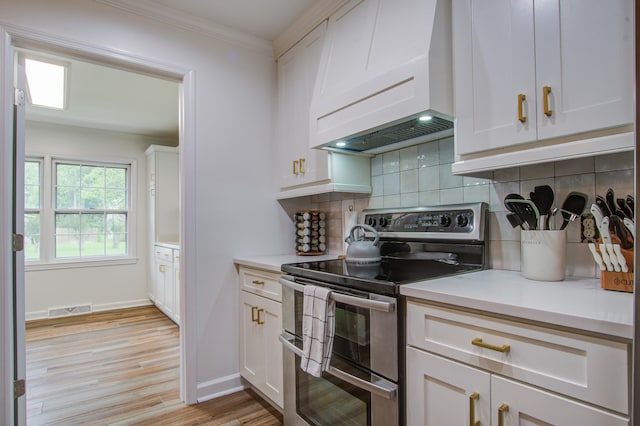 kitchen with white cabinets, light hardwood / wood-style flooring, electric range, custom exhaust hood, and ornamental molding