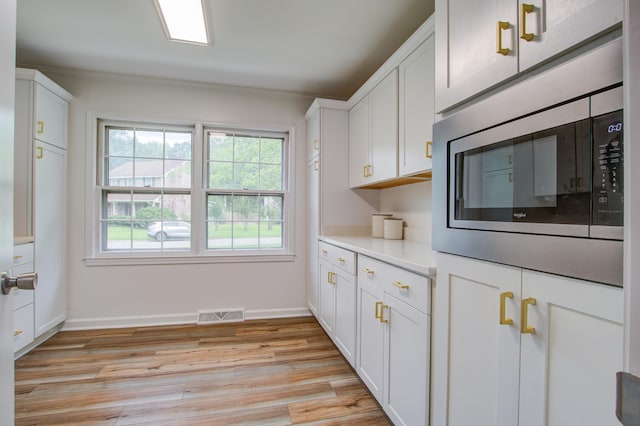 kitchen featuring light wood-type flooring, white cabinets, crown molding, and stainless steel microwave