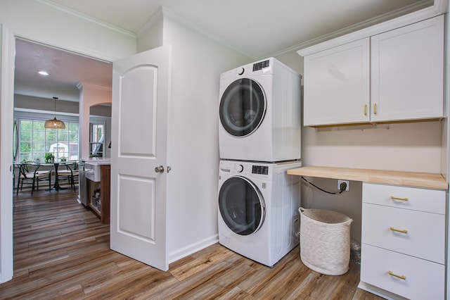 clothes washing area with stacked washer and clothes dryer, crown molding, cabinets, and light hardwood / wood-style flooring