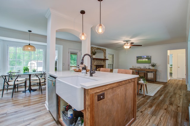 kitchen with hanging light fixtures, a brick fireplace, light hardwood / wood-style floors, an island with sink, and ceiling fan