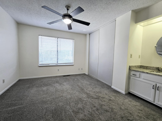 unfurnished bedroom with ceiling fan, sink, a textured ceiling, and dark colored carpet