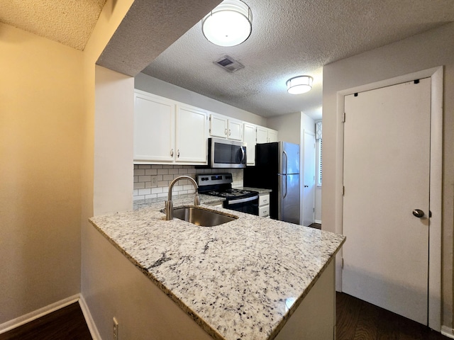 kitchen with sink, kitchen peninsula, appliances with stainless steel finishes, tasteful backsplash, and white cabinetry