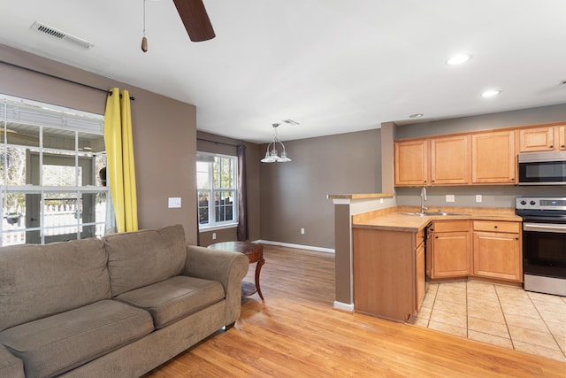 kitchen featuring appliances with stainless steel finishes, decorative light fixtures, sink, kitchen peninsula, and light hardwood / wood-style flooring