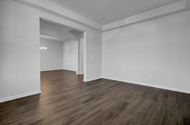 spare room featuring dark wood-type flooring and a notable chandelier