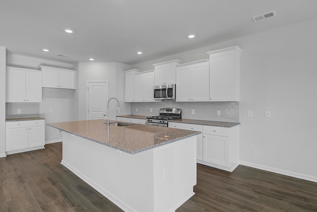 kitchen with white cabinetry, appliances with stainless steel finishes, an island with sink, and dark hardwood / wood-style floors