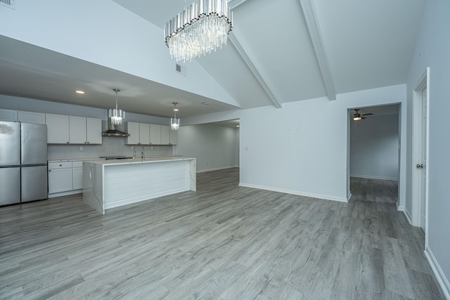 kitchen with light wood-type flooring, stainless steel refrigerator, white cabinetry, an island with sink, and wall chimney exhaust hood