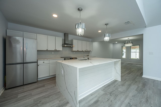 kitchen with a kitchen island with sink, wall chimney exhaust hood, white cabinetry, and stainless steel appliances