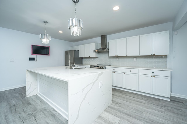 kitchen with wall chimney range hood, a center island with sink, and white cabinetry