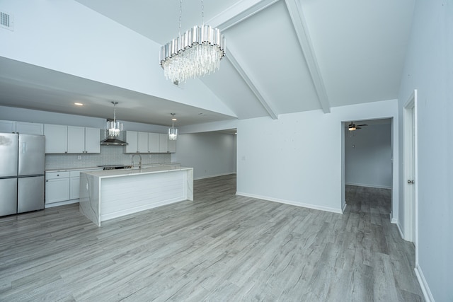 kitchen with decorative light fixtures, stainless steel appliances, white cabinetry, wall chimney range hood, and a kitchen island with sink