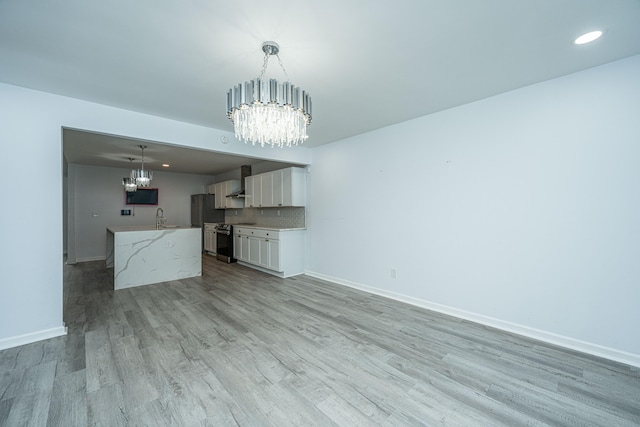 unfurnished living room featuring sink, light wood-type flooring, and a chandelier