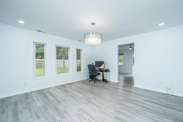 empty room featuring ceiling fan with notable chandelier and light hardwood / wood-style floors