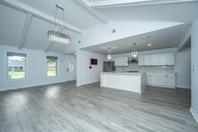 kitchen with decorative light fixtures, light hardwood / wood-style floors, white cabinetry, wall chimney exhaust hood, and a center island with sink