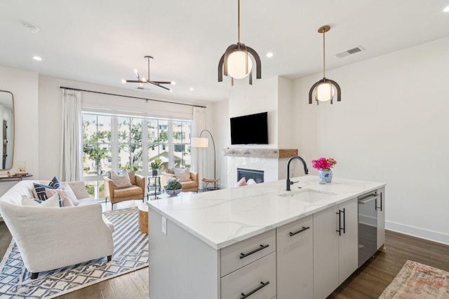 kitchen with a kitchen island with sink, white cabinets, hanging light fixtures, dark hardwood / wood-style floors, and light stone counters