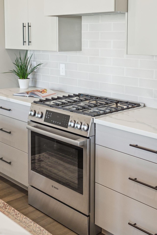 kitchen with decorative backsplash, light stone counters, stainless steel stove, and dark wood-type flooring