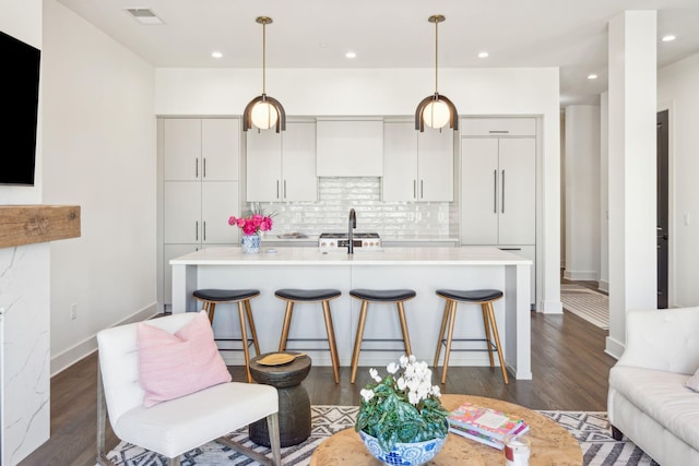 kitchen featuring dark hardwood / wood-style flooring, tasteful backsplash, a breakfast bar, pendant lighting, and a center island with sink