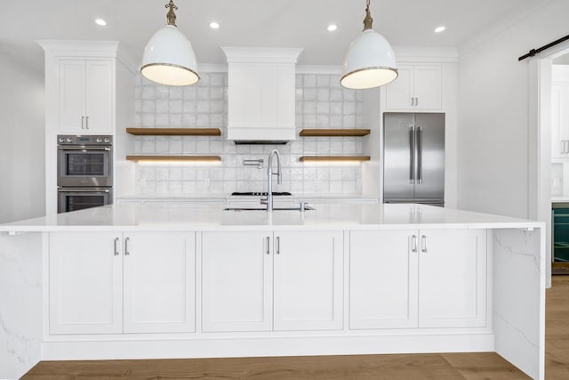 kitchen featuring a large island with sink, decorative light fixtures, stainless steel appliances, and white cabinets