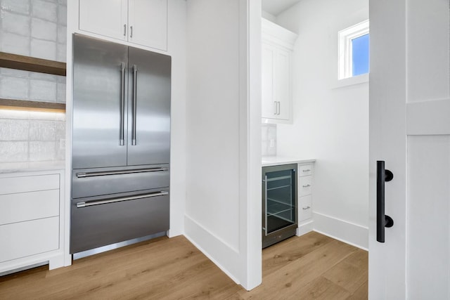 kitchen featuring beverage cooler, stainless steel built in fridge, light hardwood / wood-style flooring, and white cabinets