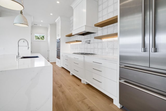 kitchen with sink, hanging light fixtures, stainless steel appliances, light stone countertops, and custom range hood