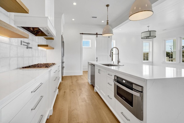 kitchen featuring sink, hanging light fixtures, an island with sink, a barn door, and white cabinets