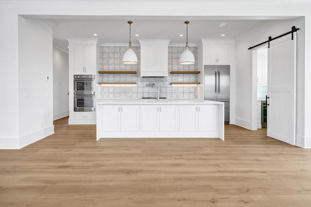 kitchen with stainless steel appliances, a barn door, hanging light fixtures, and white cabinets