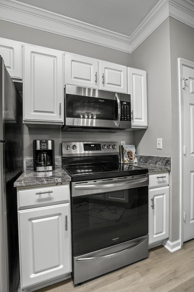 kitchen with white cabinetry, dark stone countertops, light wood-type flooring, appliances with stainless steel finishes, and ornamental molding