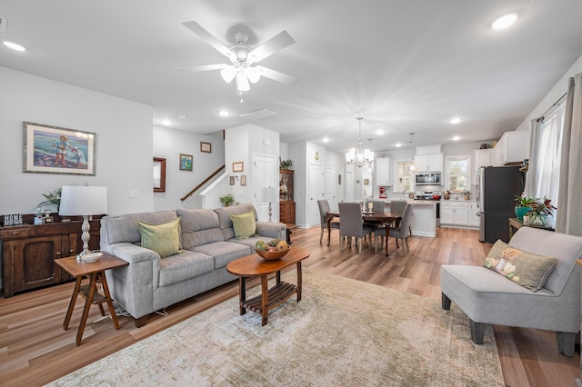 living room with light wood-style flooring, ceiling fan with notable chandelier, stairway, and recessed lighting