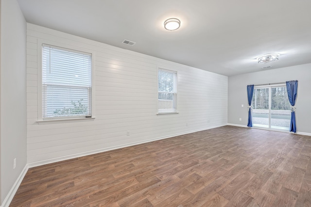 unfurnished room with visible vents, wooden walls, baseboards, and wood finished floors