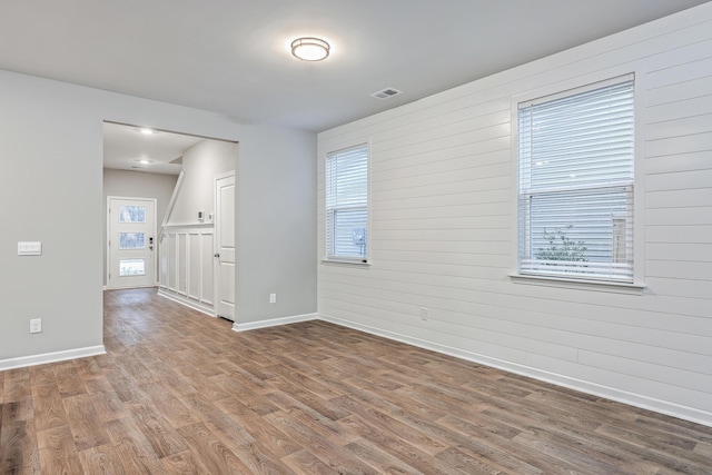 spare room featuring baseboards, wooden walls, visible vents, and wood finished floors