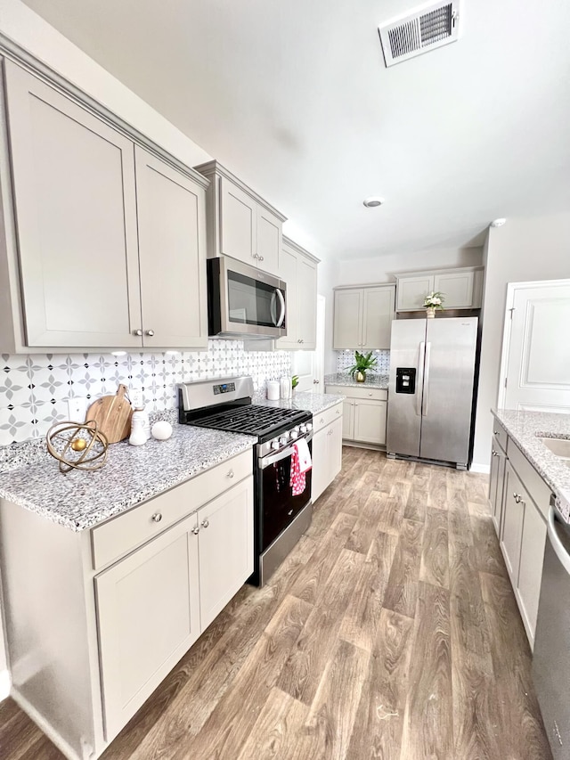 kitchen featuring gray cabinetry, appliances with stainless steel finishes, light stone countertops, light hardwood / wood-style floors, and backsplash