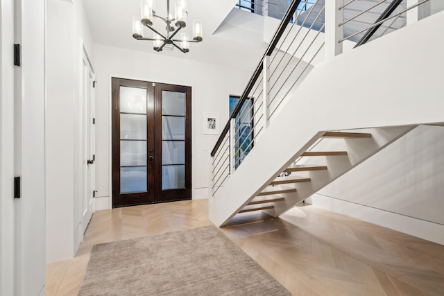 foyer featuring a towering ceiling, light parquet flooring, french doors, and a chandelier