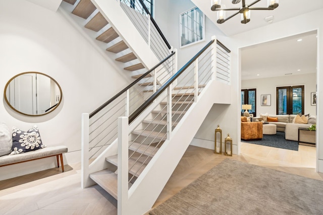 stairs featuring a high ceiling, parquet floors, a healthy amount of sunlight, and a notable chandelier