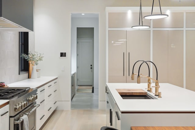 kitchen with sink, white cabinetry, high end stove, a center island with sink, and pendant lighting