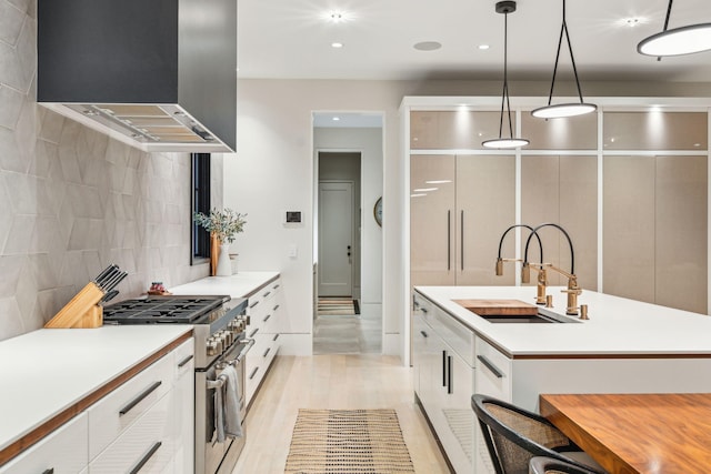 kitchen featuring extractor fan, high end range, decorative light fixtures, white cabinets, and sink