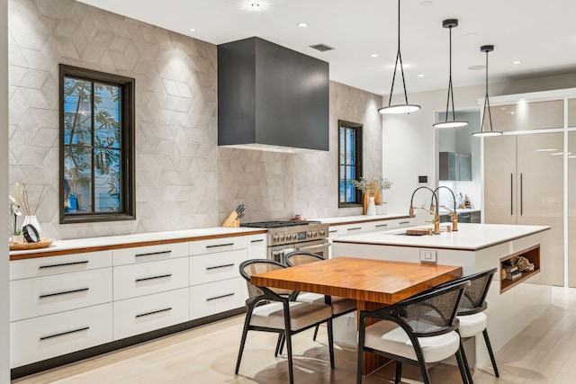 kitchen featuring a center island with sink, pendant lighting, wall chimney exhaust hood, white cabinets, and sink