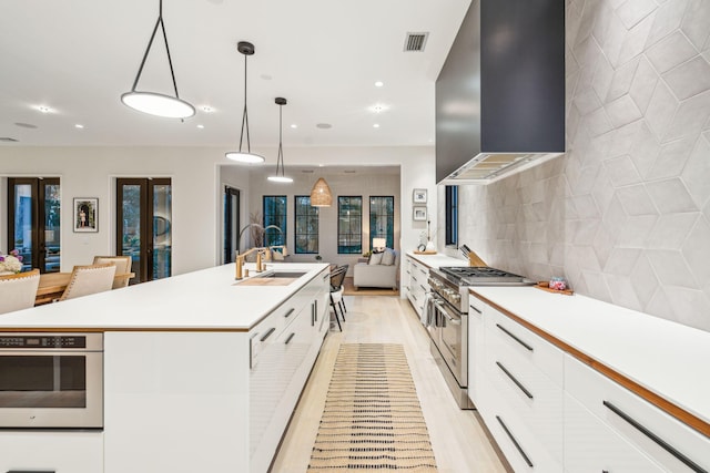 kitchen with white cabinets, a kitchen island with sink, wall chimney exhaust hood, and hanging light fixtures