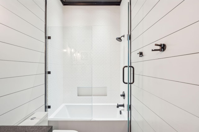 bathroom featuring toilet, enclosed tub / shower combo, and wooden walls