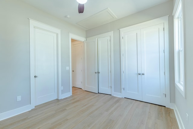 unfurnished bedroom featuring attic access, baseboards, ceiling fan, and wood finished floors