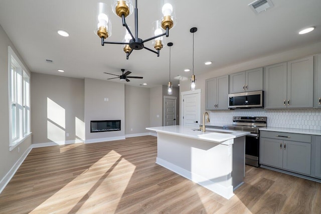 kitchen with a glass covered fireplace, backsplash, gray cabinetry, and stainless steel appliances