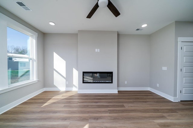 unfurnished living room featuring visible vents, wood finished floors, baseboards, and a glass covered fireplace