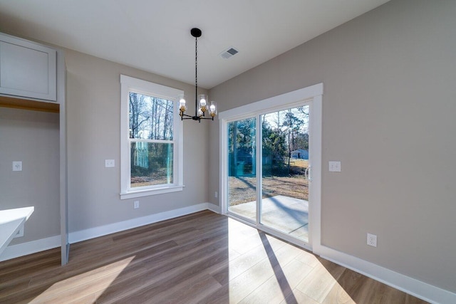 unfurnished dining area with a wealth of natural light, visible vents, dark wood-type flooring, and an inviting chandelier