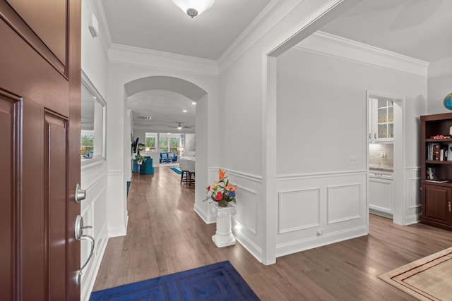entrance foyer featuring arched walkways, a decorative wall, wood finished floors, and ornamental molding